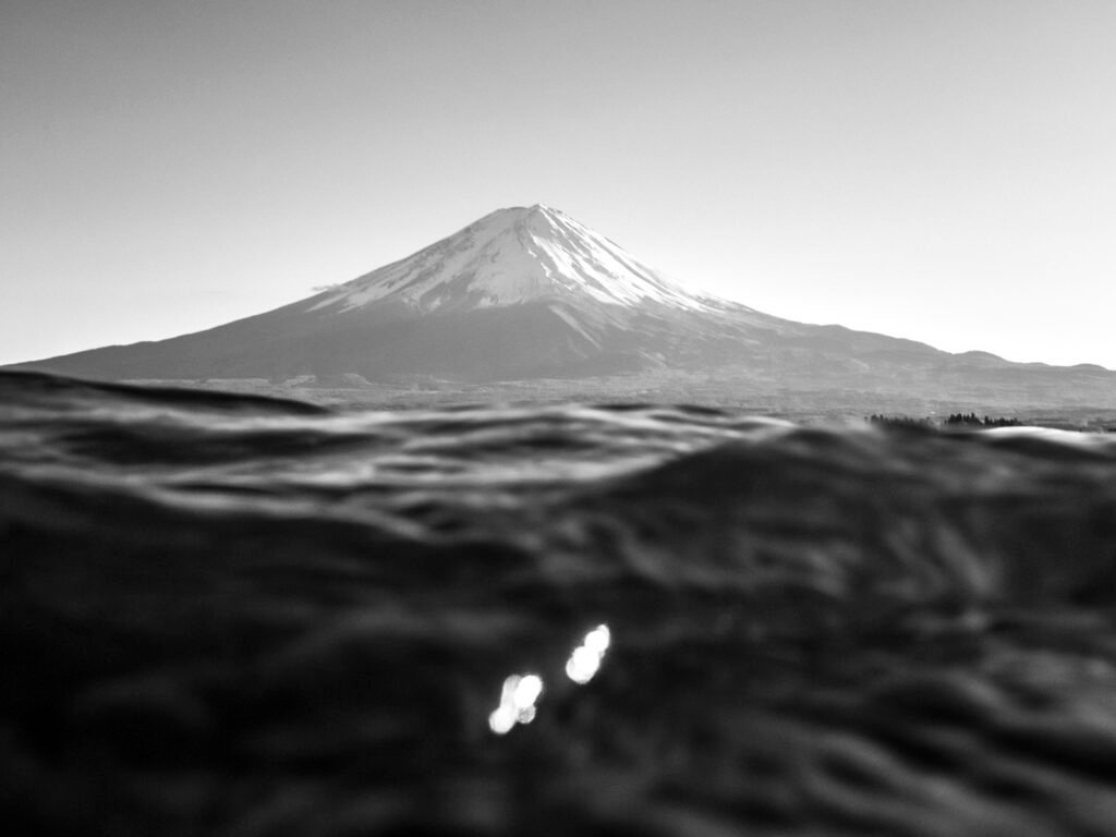 Monochrome photograph of Mt. Fuji framed by shimmering water, illustrating the interplay between permanence and transience in Japanese landscapes.